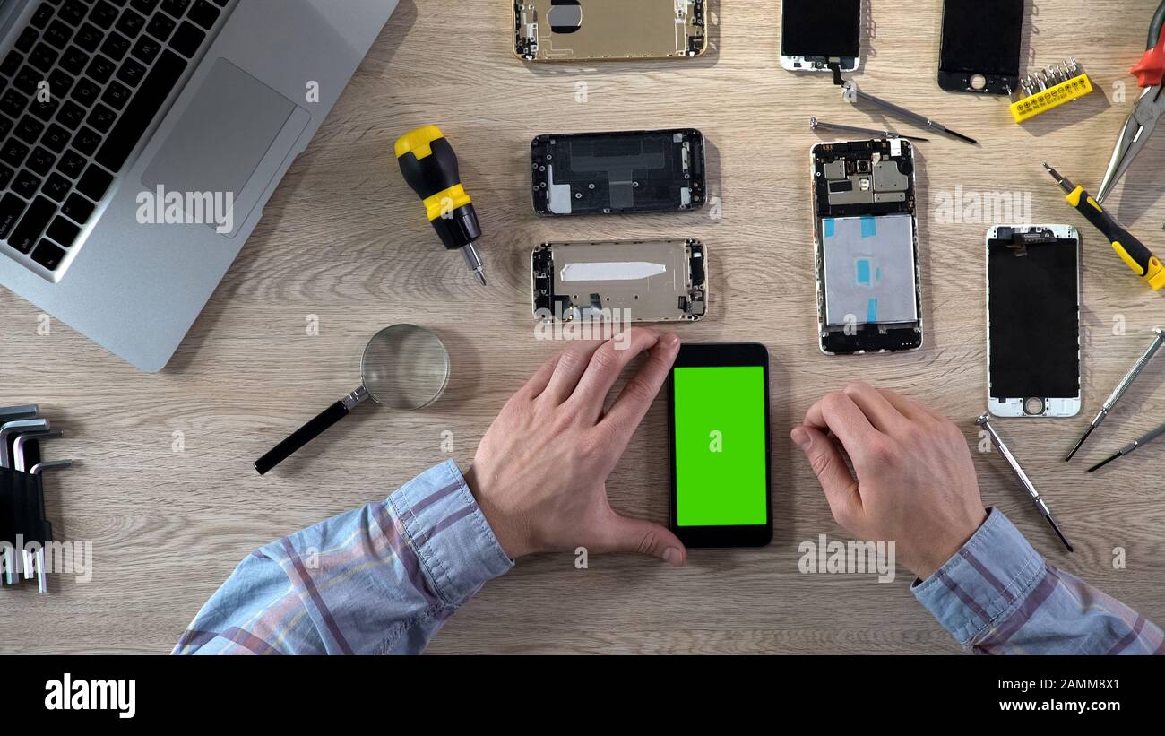 Male repairer turning on smartphone with green screen checking it after fixing Stock Photo