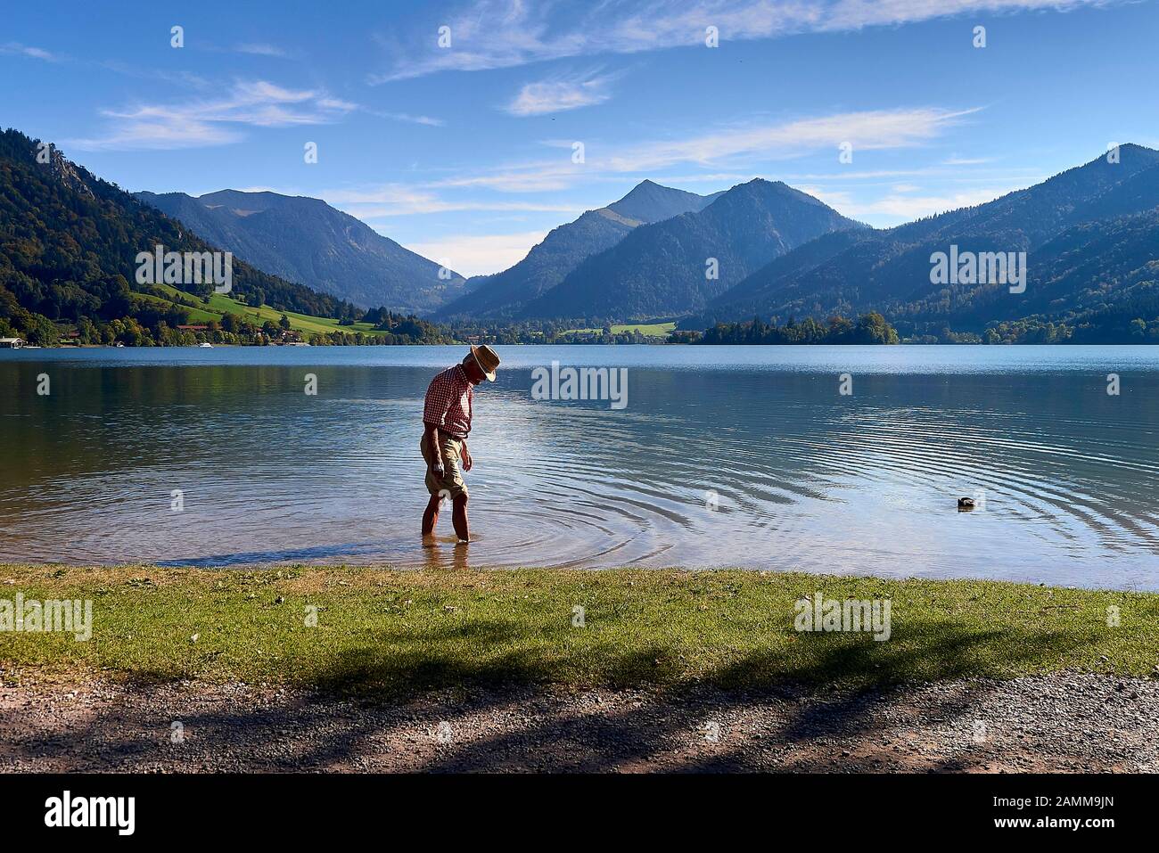Kneipp cure on the shore of the Schliersee, man with short trousers, red and white chequered shirt, straw hat, Kneipp medicine or Kneipp therapy is a treatment method named after the priest Sebastian Kneipp (1821-1897), it stimulates the circulation, promotes blood flow, strengthens the veins, helps against varicose veins, is effective against hot legs, promotes sleep when used in the evening, helps with migraines. stimulates the metabolism, strengthens the immune system, has a vegetative stabilising effect29.09.2016 [automated translation] Stock Photo