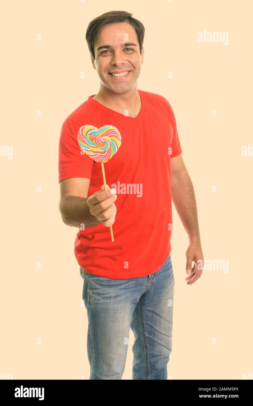 Studio shot of young happy Persian man smiling while standing and ...