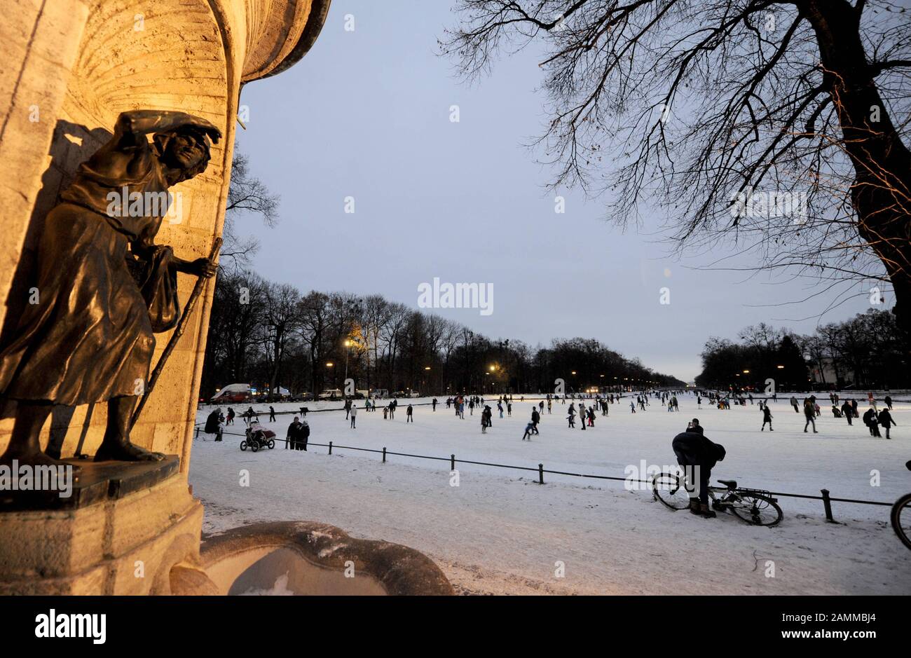 People skating on the frozen Nymphenburg Castle Canal. In the foreground the Hubertus Fountain. [automated translation] Stock Photo