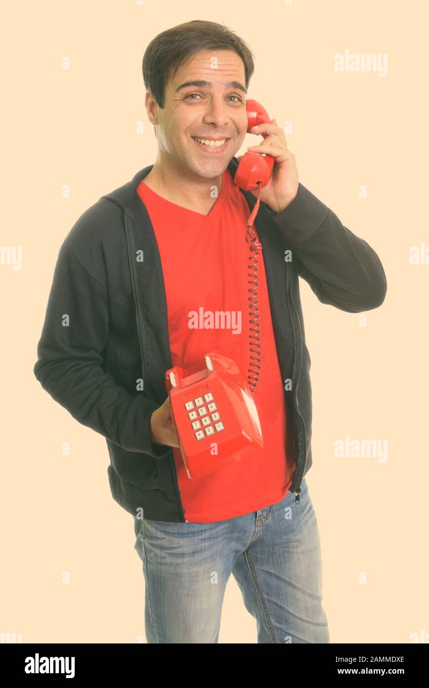 Studio shot of young happy Persian man smiling and standing while ...