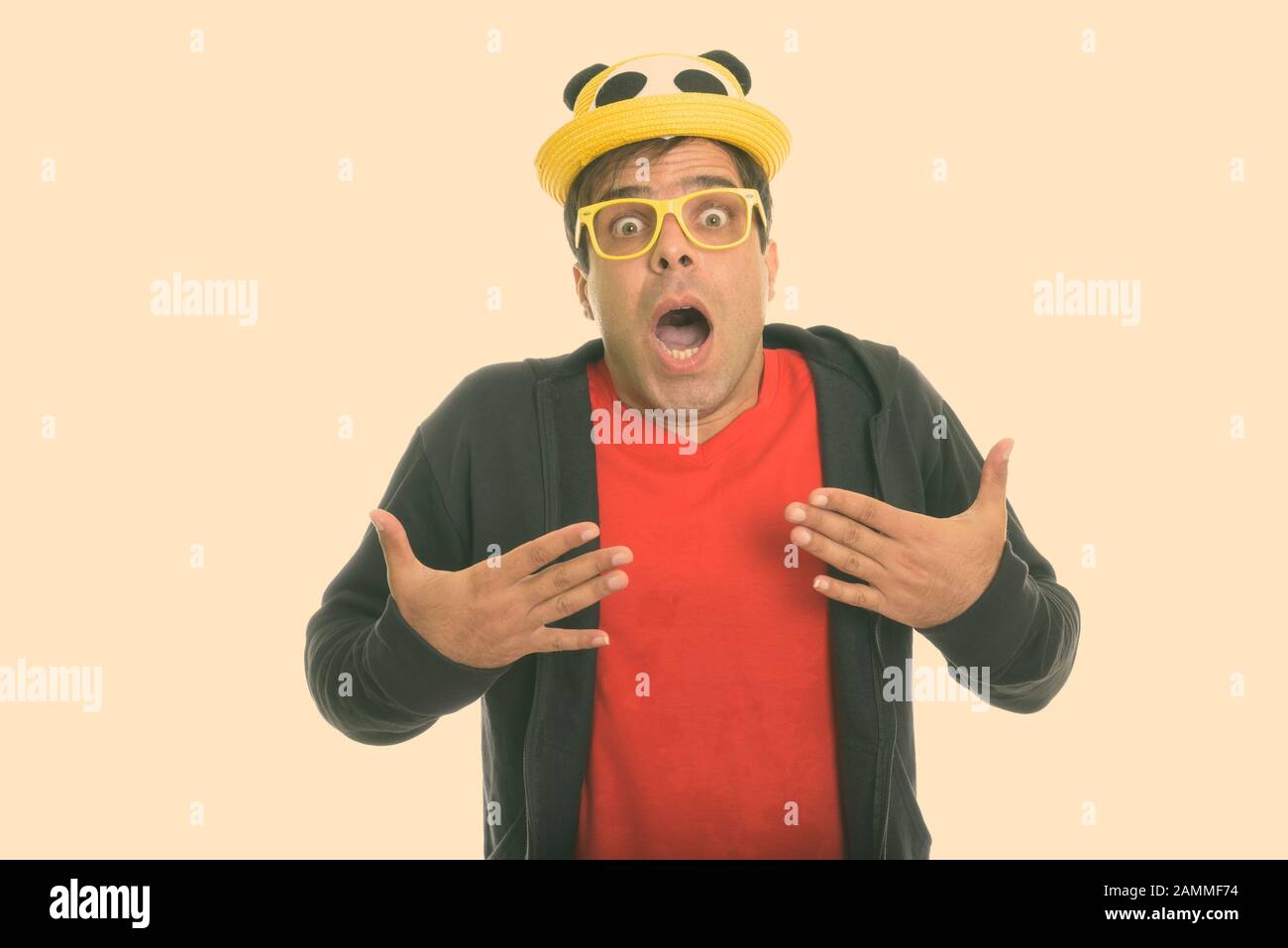 Persian man looking shocked while wearing cute hat and yellow eyeglasses Stock Photo