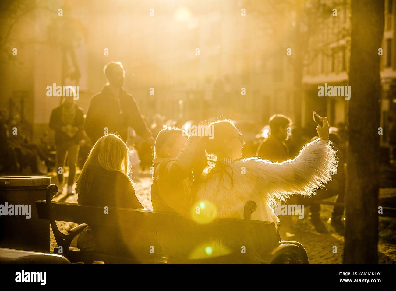 Passers-by sit in the sun at Gärtnerplatz in Munich and take pictures of themselves. [automated translation] Stock Photo