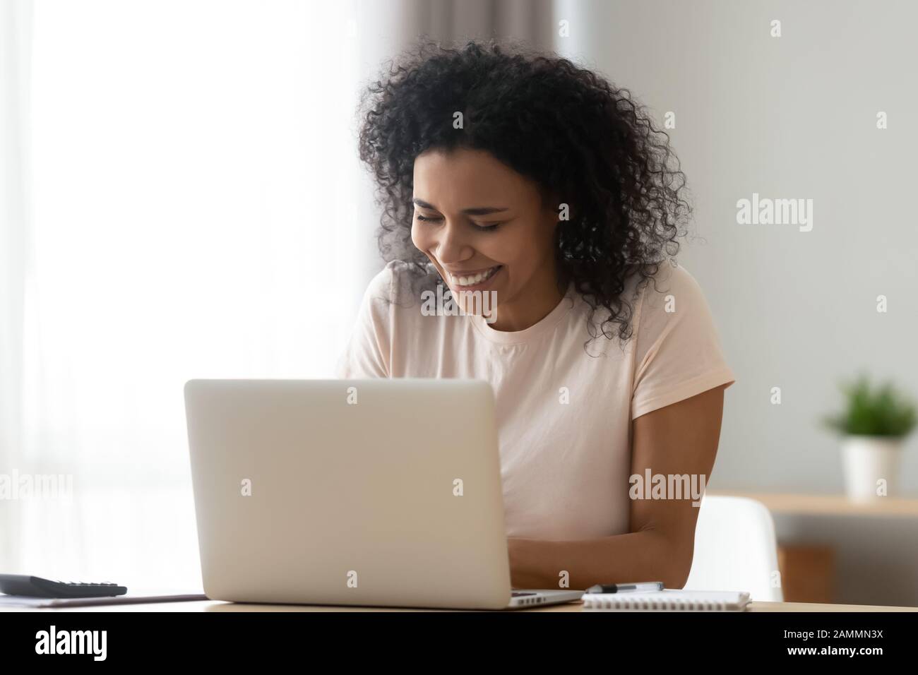African woman sitting at desk laughing chatting with friend online Stock Photo