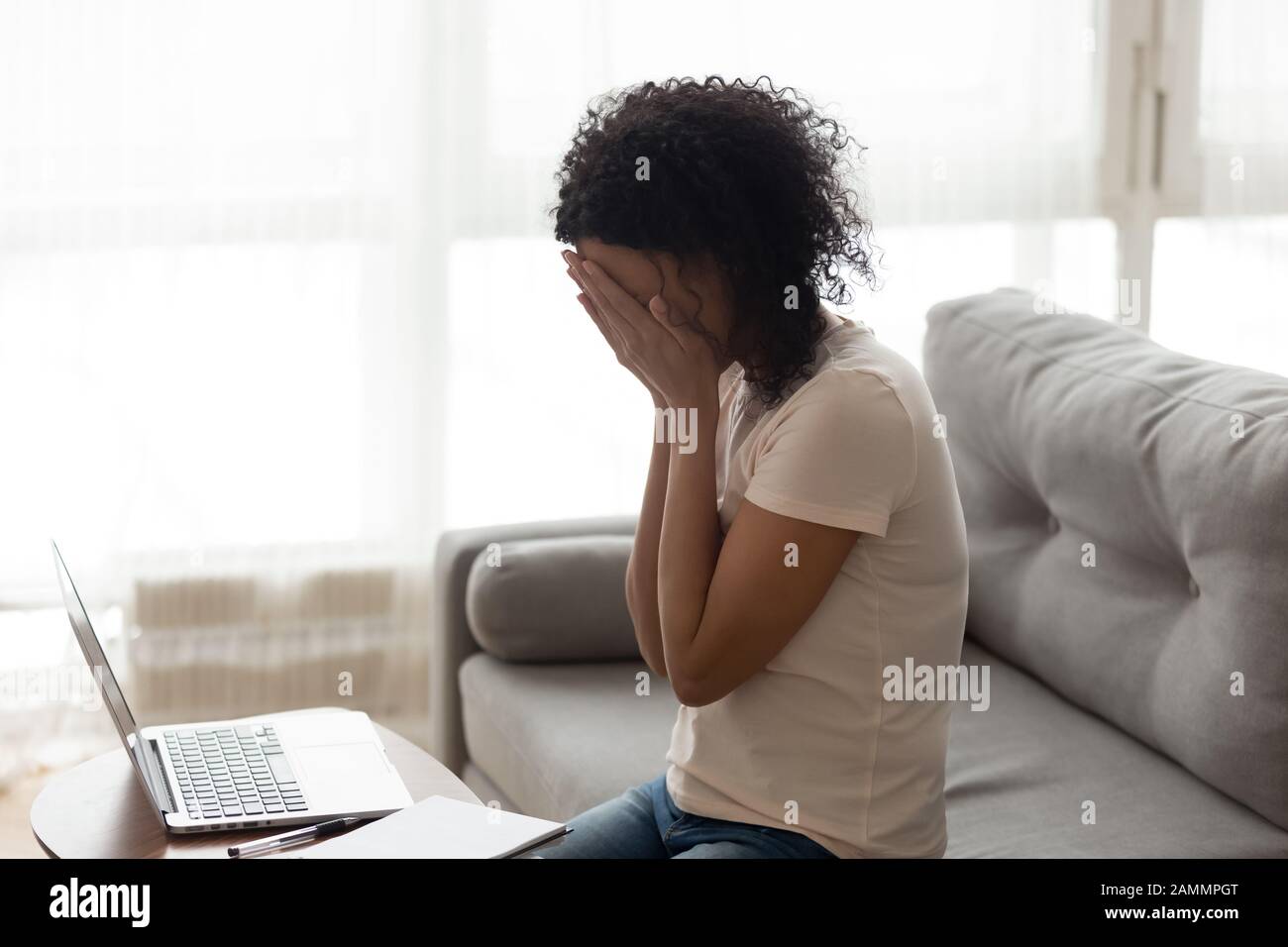 African woman sitting near computer cover face with hands crying Stock Photo