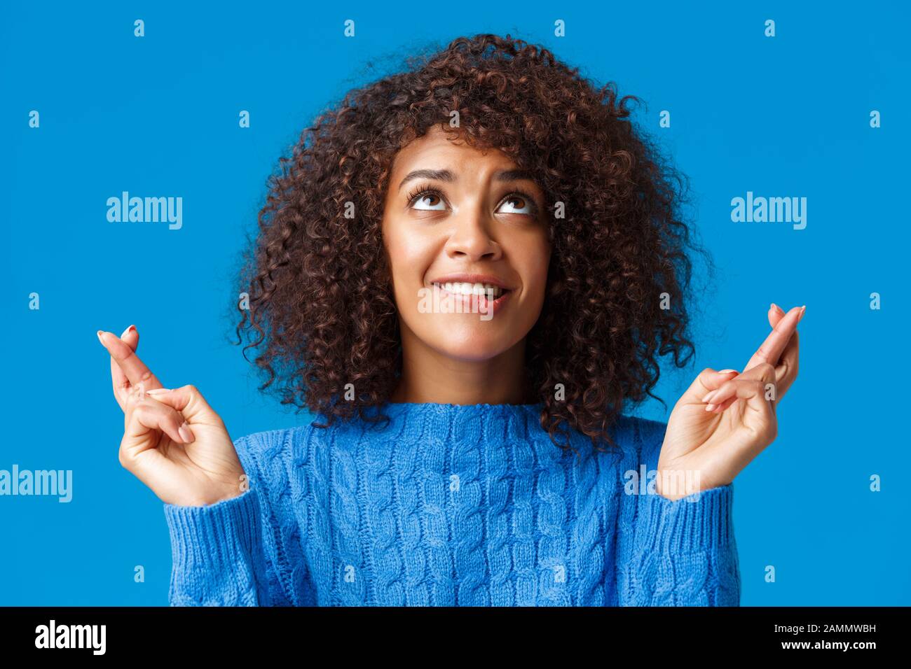 Girl begging god her dream come true. Cute and silly african-american curly-haired female with afro haircut, biting lip from temptation and desire Stock Photo