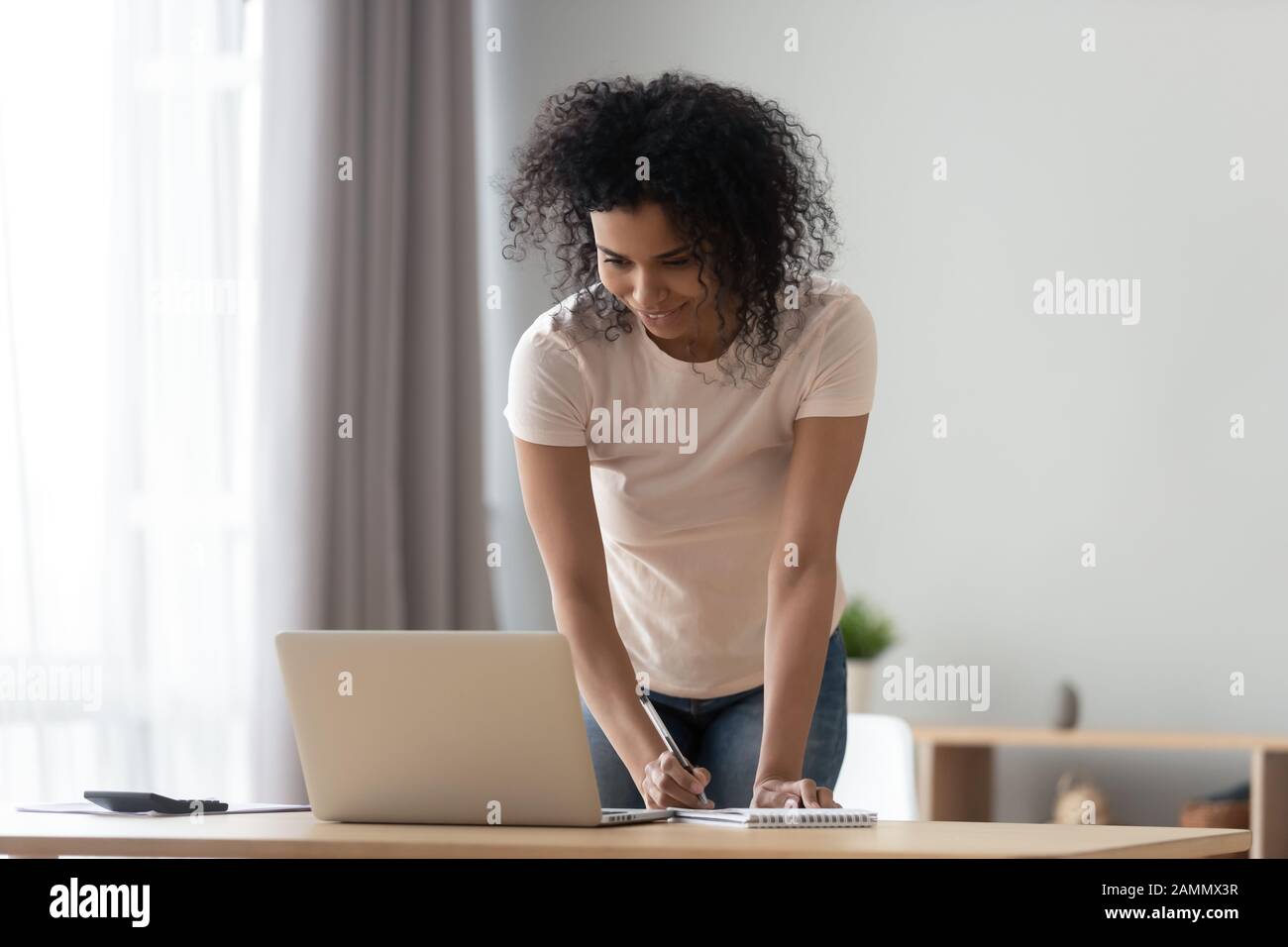 African woman looking at computer writing down useful important information Stock Photo