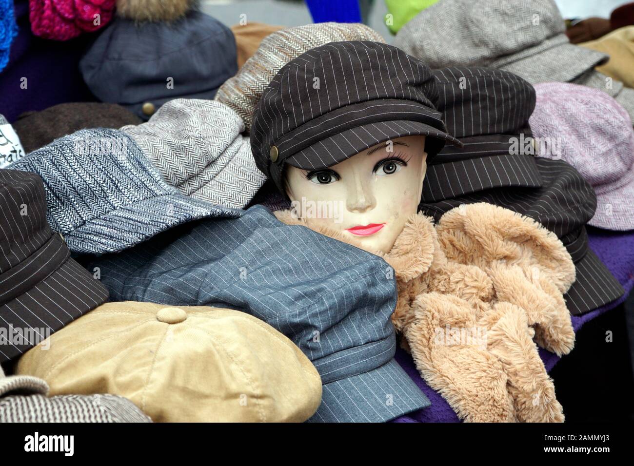 A manikin head models a hat on a market stall among other choices for Sale. Stock Photo