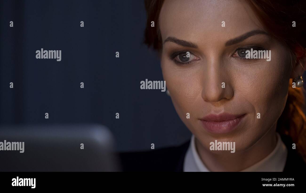 Beautiful business lady working on laptop, looking on screen at night office Stock Photo