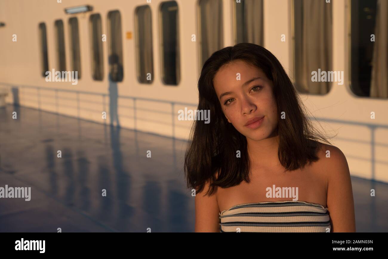 Closeup of Asian teen on in tube top on Ferry boat with windows in the background on ferry going to Lesvos Stock Photo