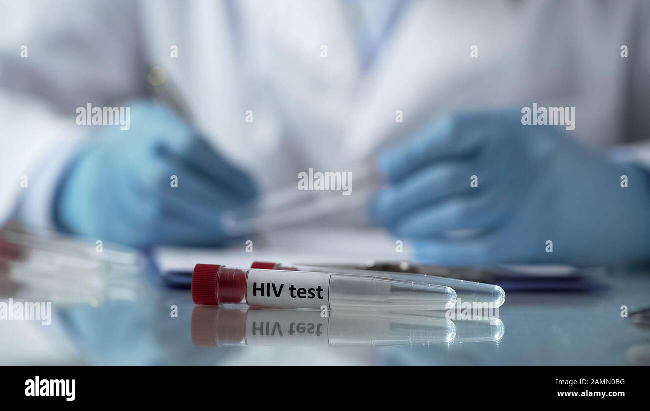 Lab worker filling in test results forms, holding plastic tube with HIV ...