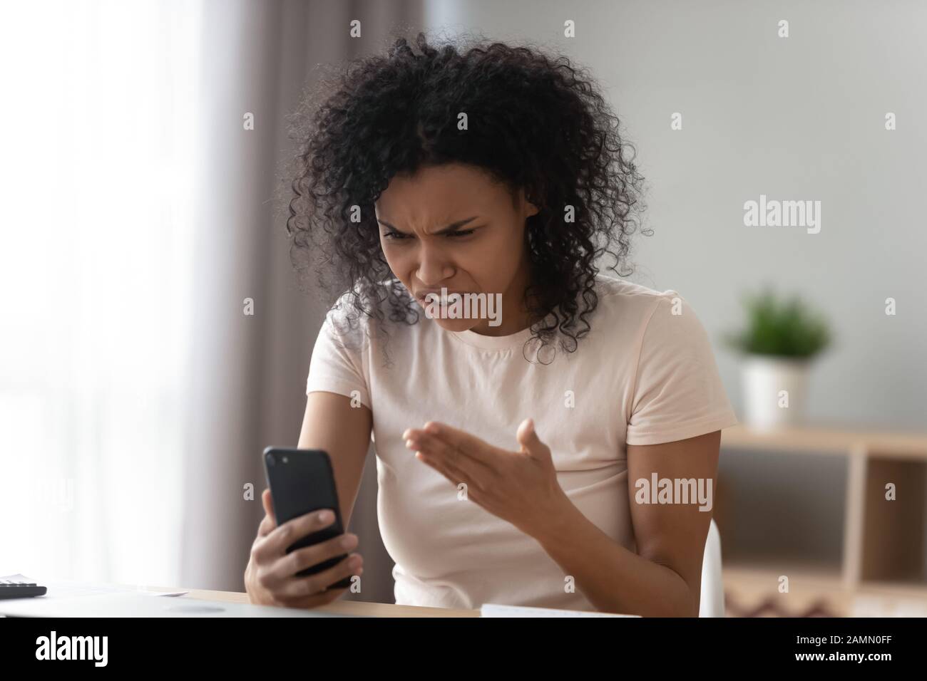 African woman holding smartphone looks at screen swears on gadget Stock ...