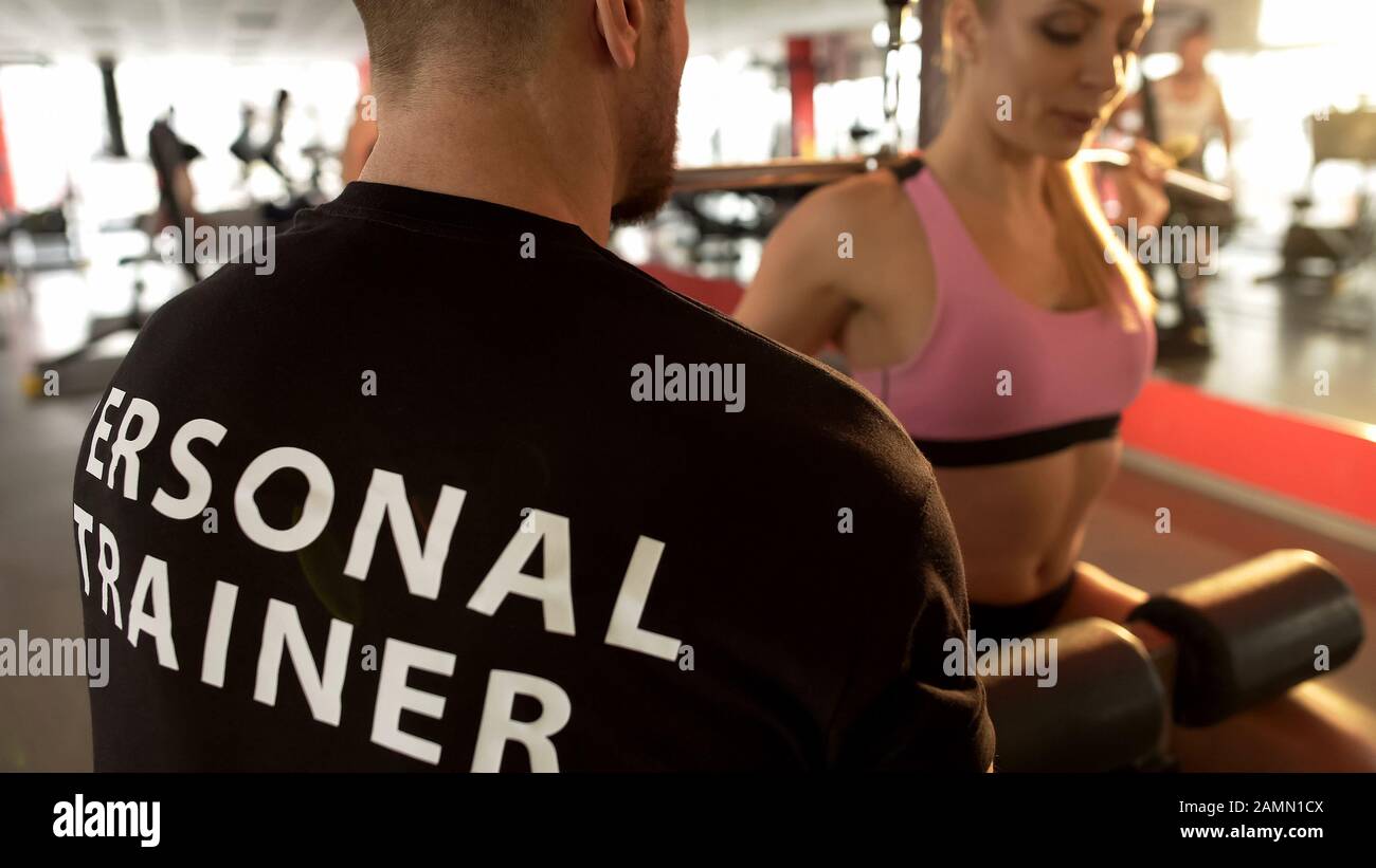 Fit female doing rear lat pull-down under supervision of her personal  trainer Stock Photo - Alamy