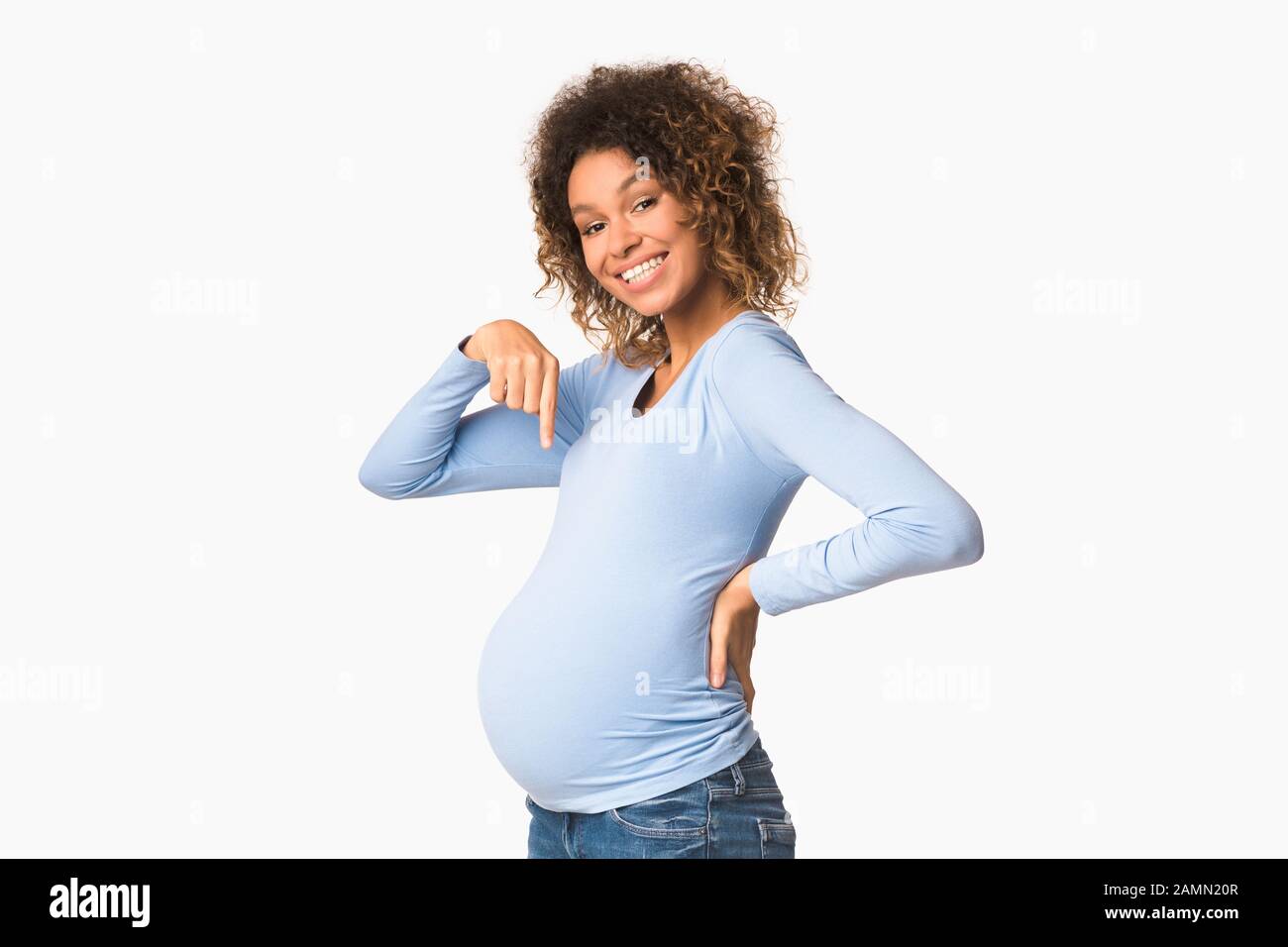 Excited afro pregnant woman pointing finger at belly Stock Photo