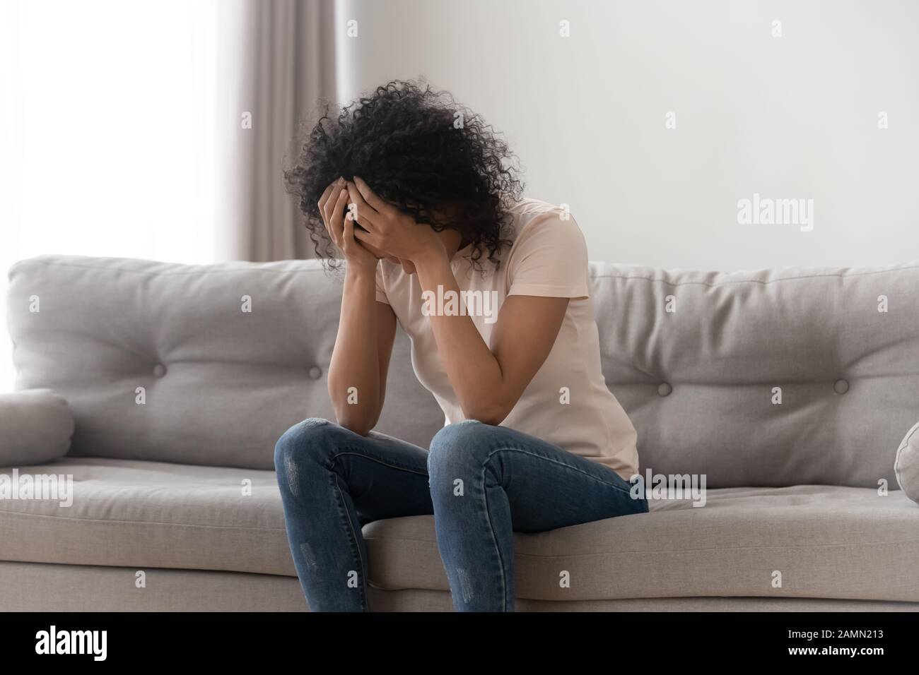 African woman cover face with hands crying sitting on couch Stock Photo