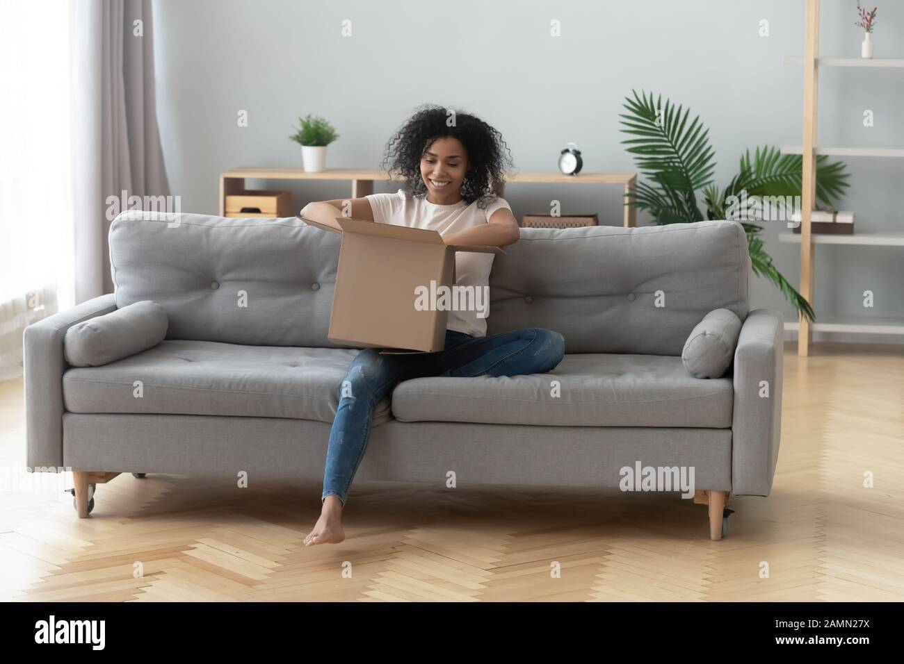 African woman sitting on couch unpacking received parcel feels happy Stock Photo