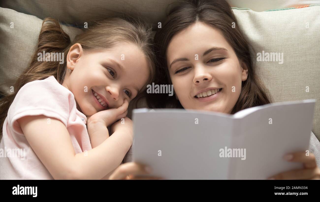 Loving young mother reading book to smiling cute little daughter Stock Photo