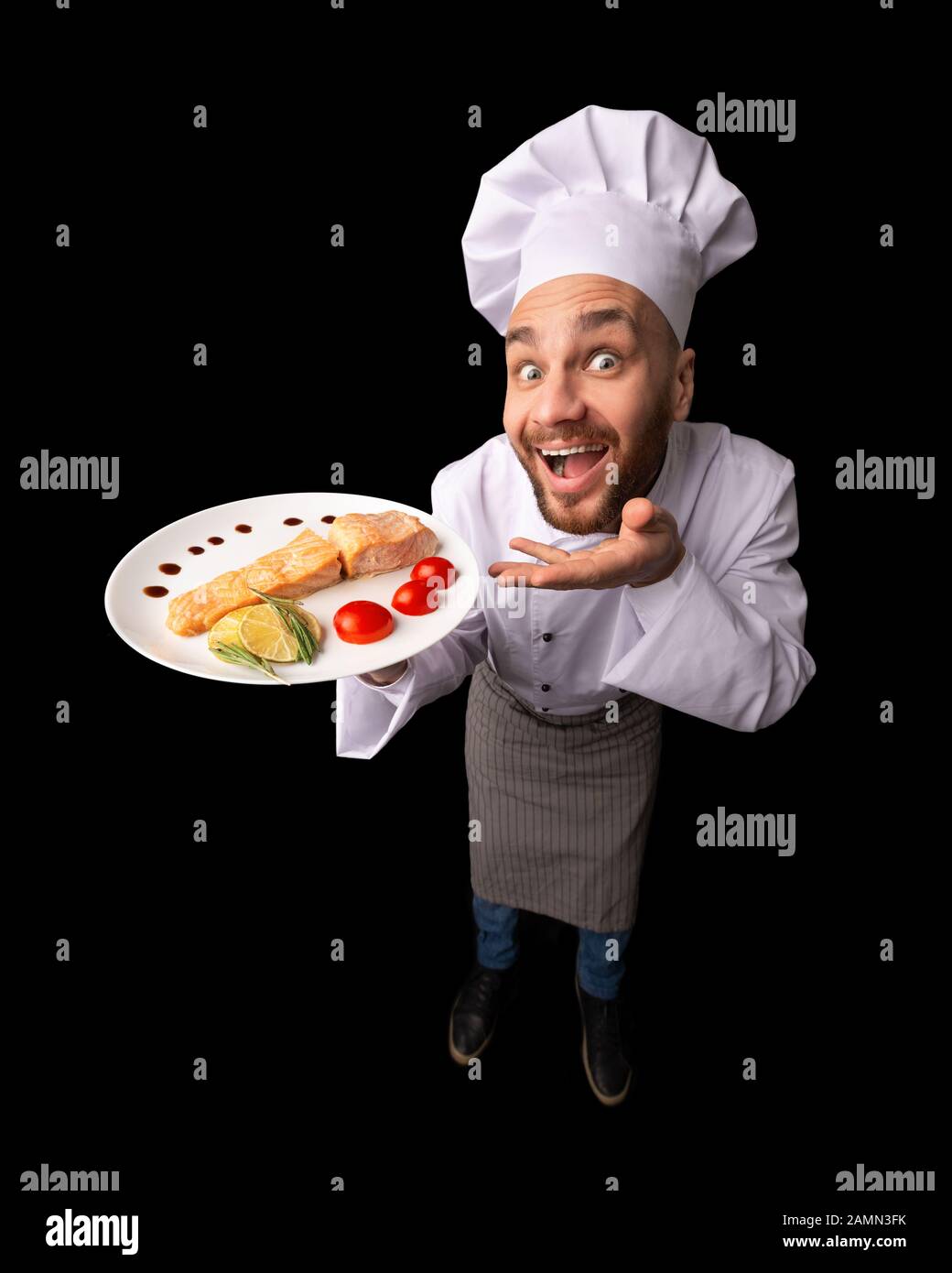 Funny Chef Guy Holding Fish Dish Standing In Studio, High-Angle Stock Photo