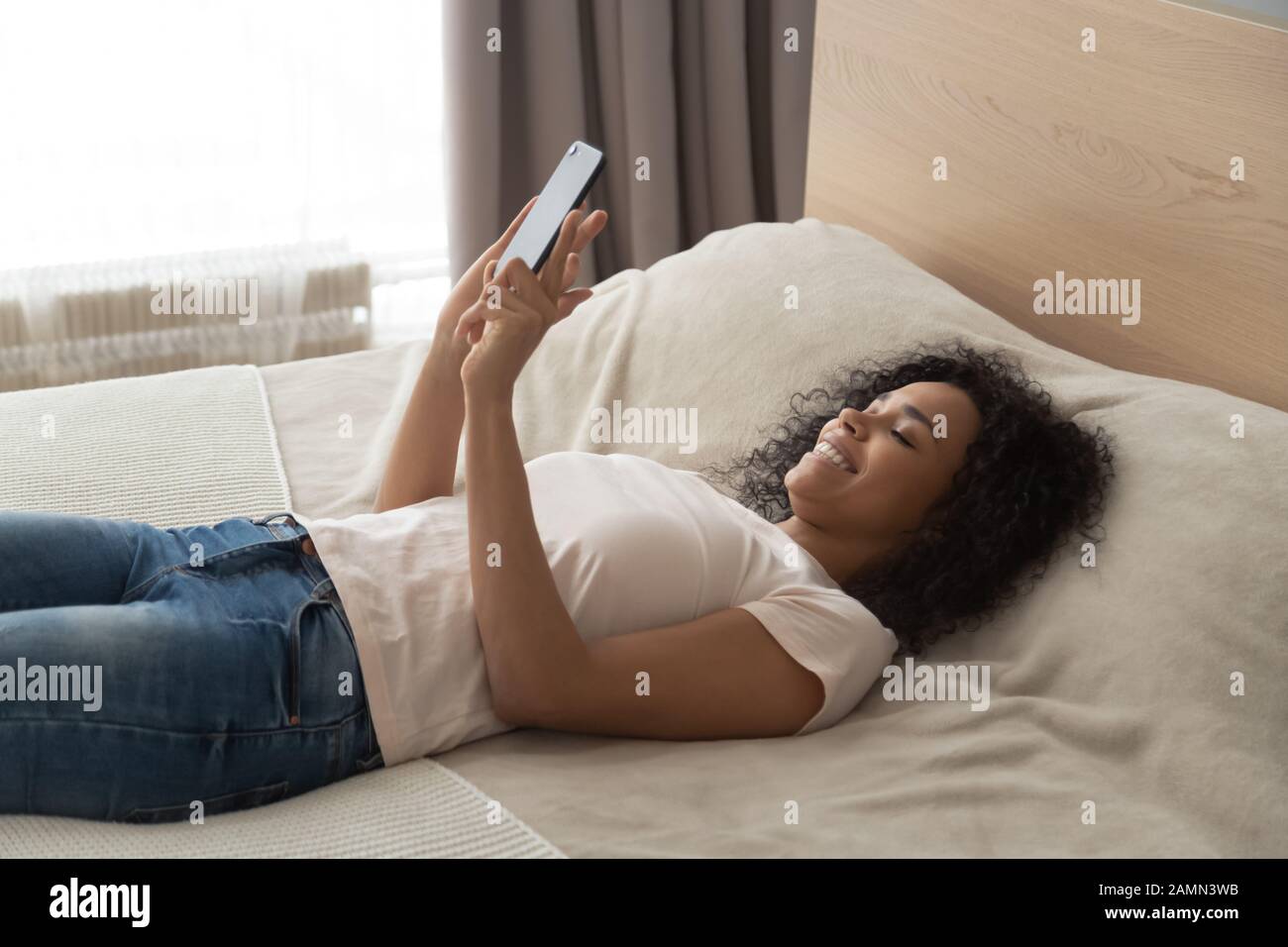 African woman lying resting in bed using smartphone applications Stock Photo