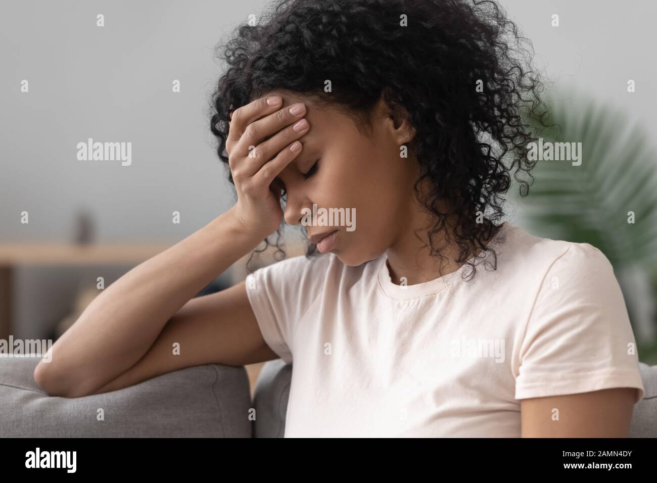 African woman sitting on couch feels unhappy having problems Stock Photo