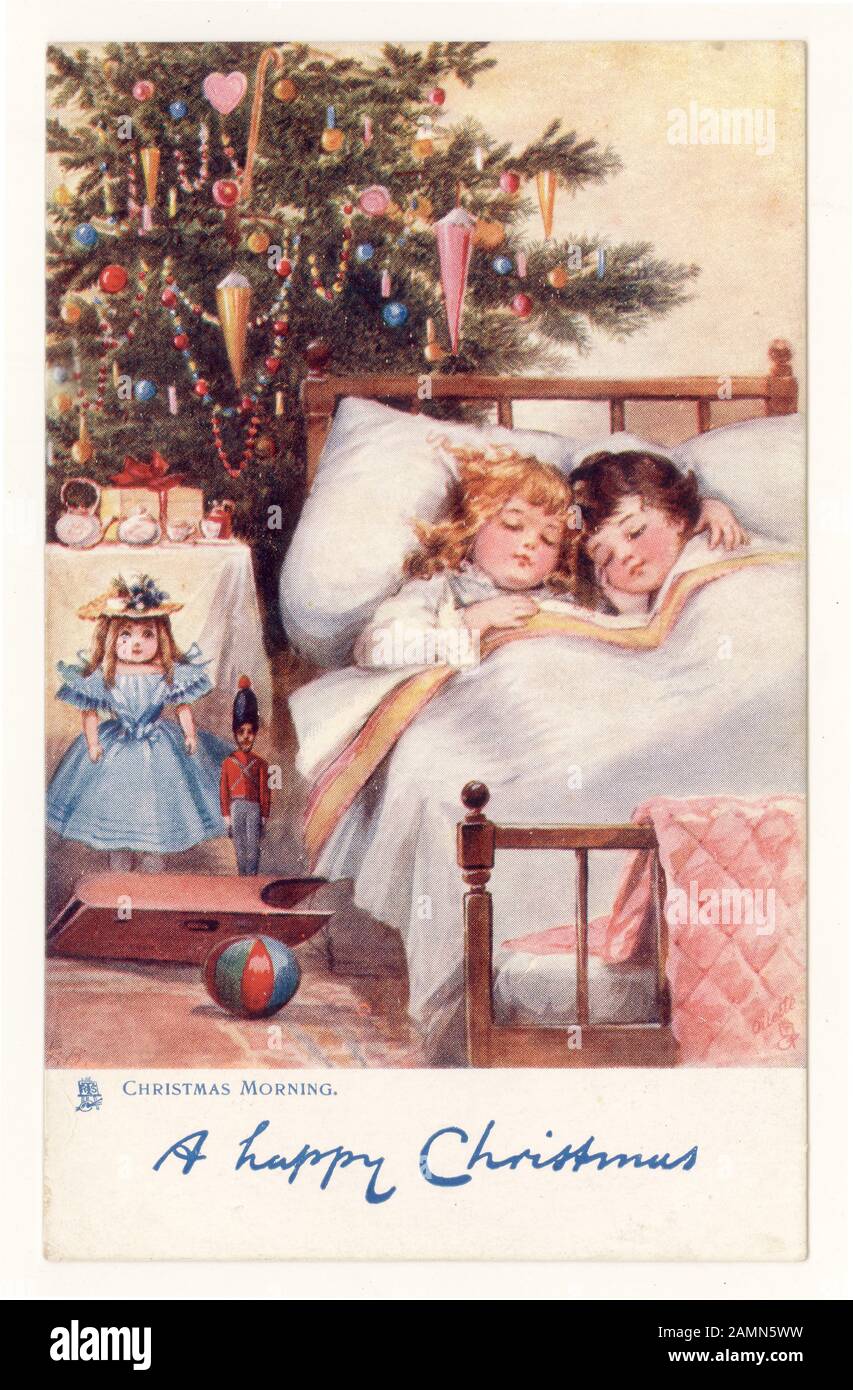 Original cute traditional Christmas greetings postcard of children tucked up in bed on Christmas morning with presents and tree, original oilette, circa 1905, England, U.K. Stock Photo