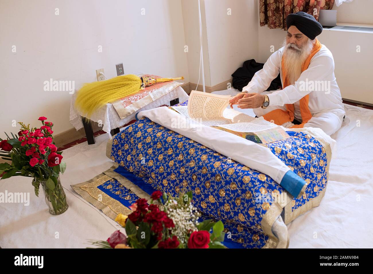 A seated Sikh priest reads from the holy scripture, the Gugru Granth Sahib. In a temple in Richmond Hill, Queens, New York City. Stock Photo