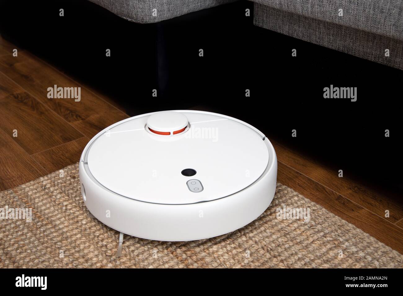 Robotic vacuum cleaner runs under sofa in room on laminate floor modern