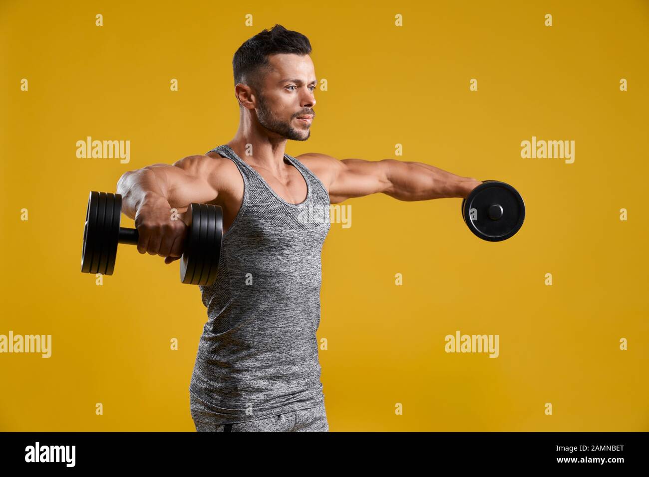 Side view of muscular gentleman lifting heavy weights. Strong
