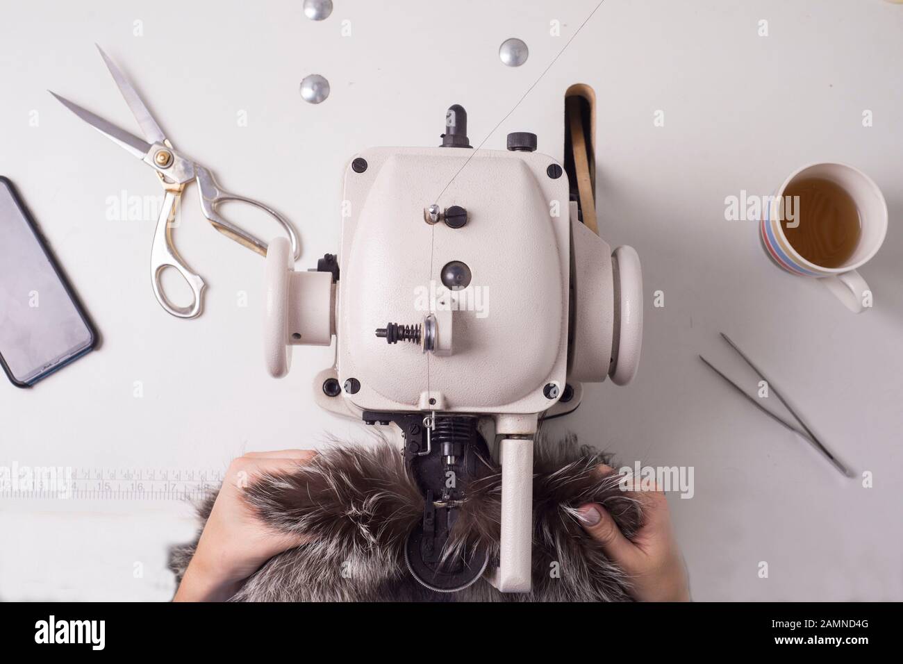 Top view of the work of a professional fur fabricator. Workplace designer sewing machine. Sewing clothes from raccoon. Animal fur, designer fur coat. Stock Photo