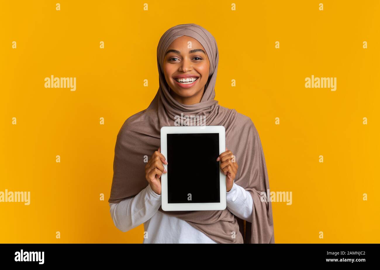 Smiling afro woman in headscarf demonstrating digital tablet with black ...