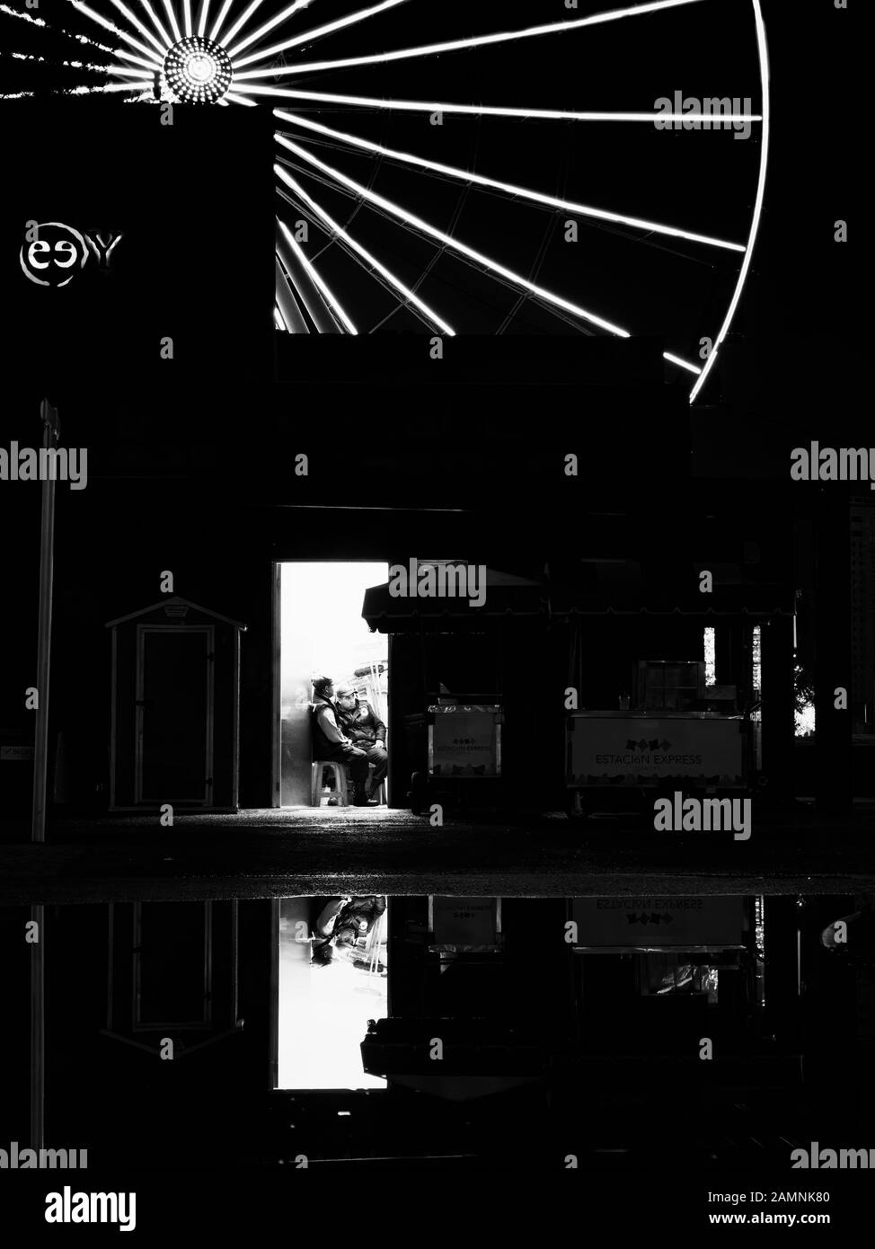 Puebla de Zaragoza, October 12, 2018 - Monochrome scene of modern building with two man and ferris wheel reflections in the water after the rain at night. Stock Photo