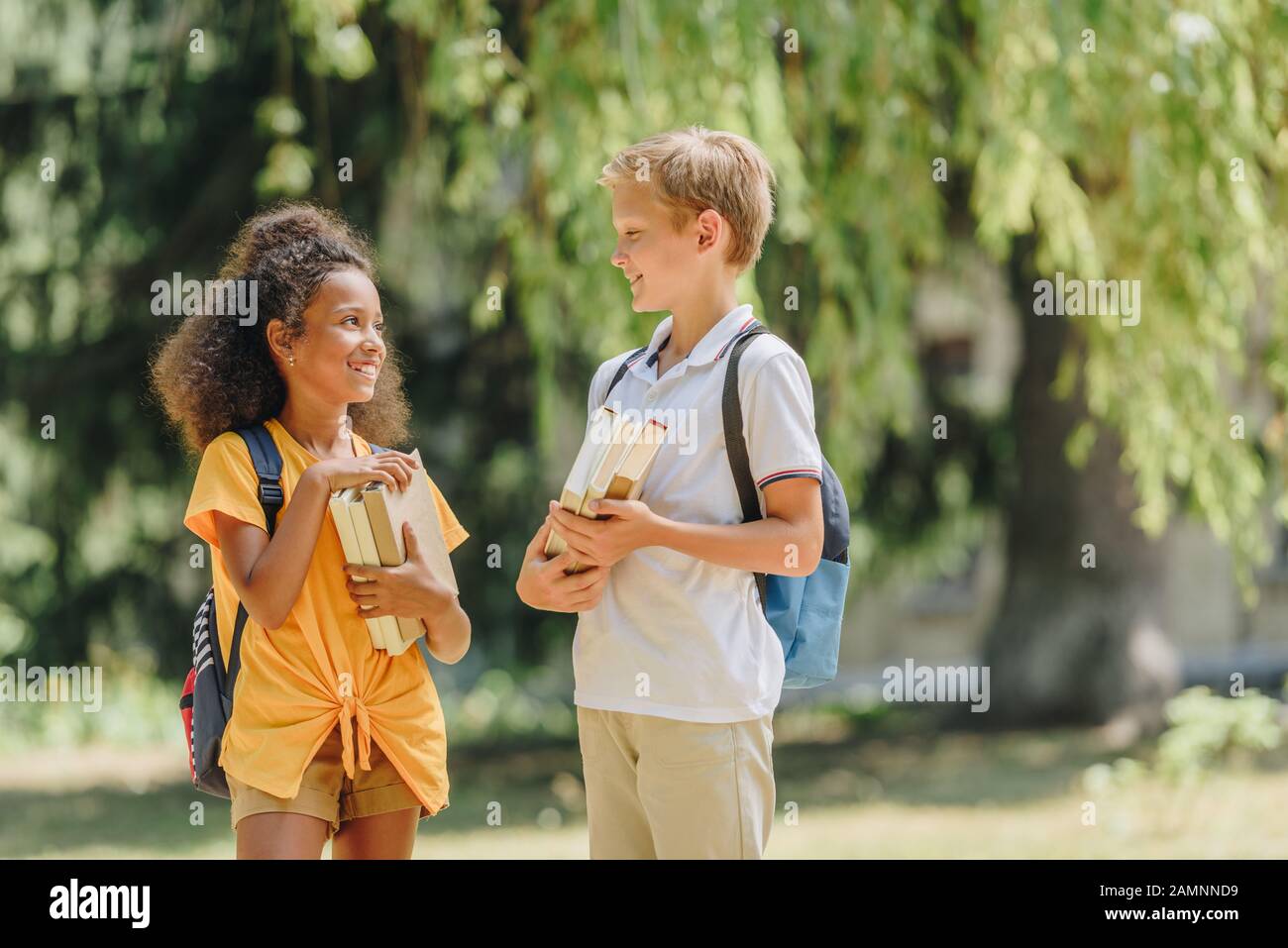 two cheerful multicultural schoolkids smiling and speaking while holding books Stock Photo