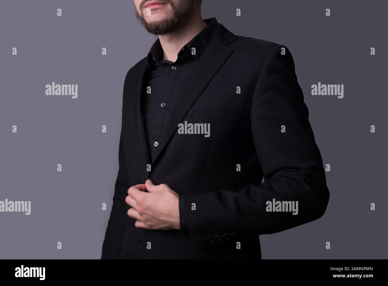 A man in a black jacket, on a dark gray background. minimalistic concept. Empty free space. Portrait of a young guy in a black business suit, holding Stock Photo