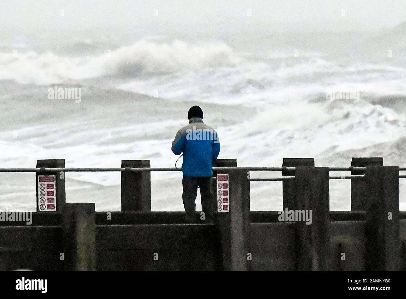 West Bay, Dorset, UK.  14th January 2020. UK Weather.   A man standing on the pier watching the rough seas at West Bay in Dorset as stormy conditions continue after Storm Brendan.  Picture Credit: Graham Hunt/Alamy Live News Stock Photo