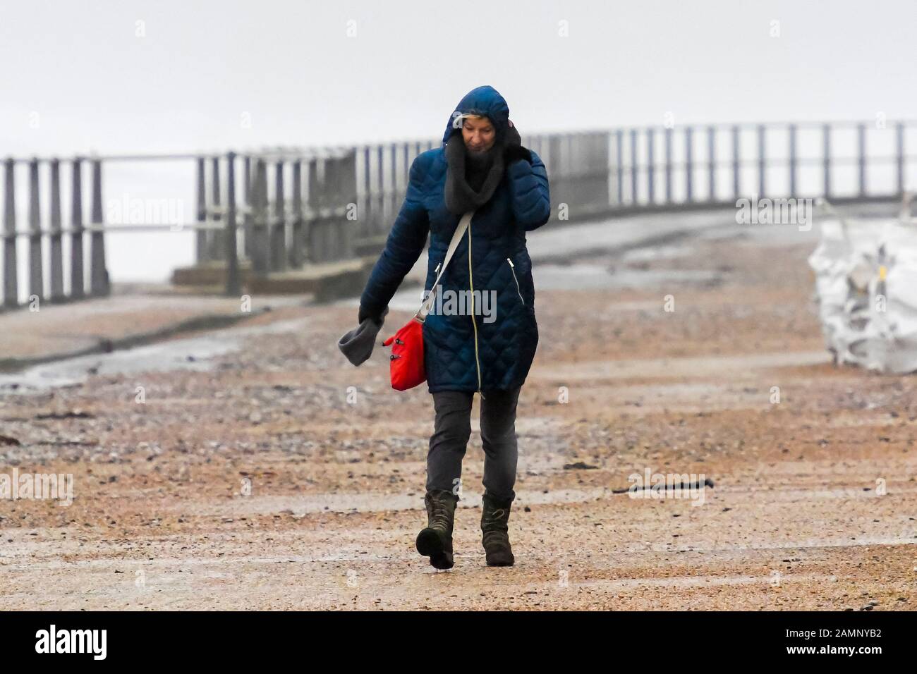 West Bay, Dorset, UK.  14th January 2020. UK Weather.  A woman struggles to walk along the seafront against the strong gusty wind at West Bay in Dorset as stormy conditions continue after Storm Brendan.  Picture Credit: Graham Hunt/Alamy Live News Stock Photo