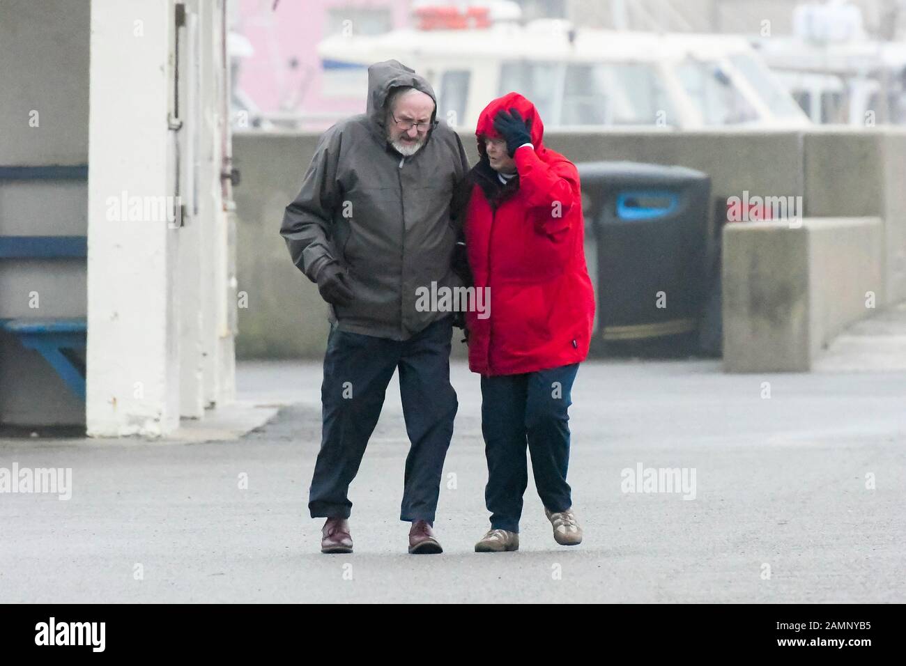 West Bay, Dorset, UK.  14th January 2020. UK Weather.  A couple struggle to walk along the seafront against the strong gusty wind at West Bay in Dorset as stormy conditions continue after Storm Brendan.  Picture Credit: Graham Hunt/Alamy Live News Stock Photo