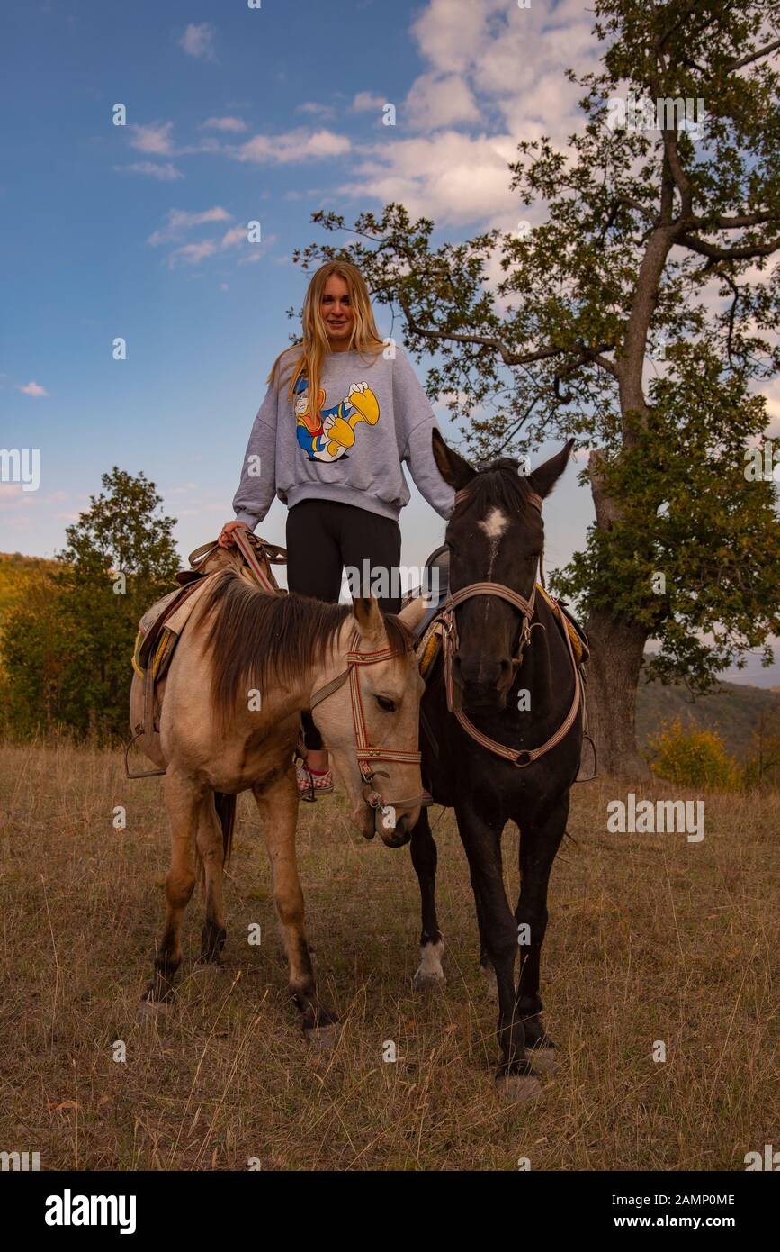 A teenage girl stands in stirrups on two horses at the same time. Stock Photo