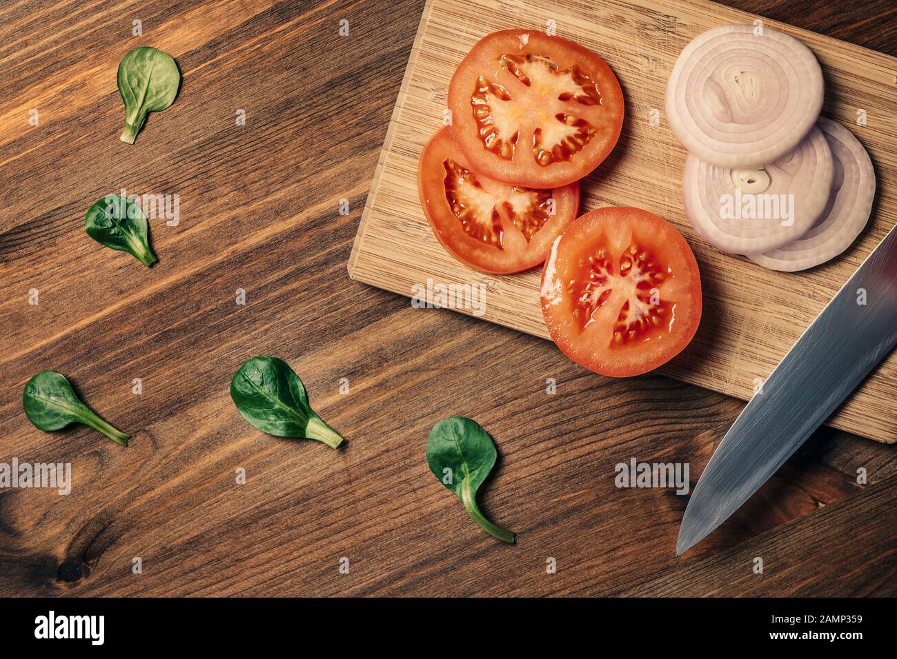 knife with slices of tomato and onion on a cutting board and some green ...