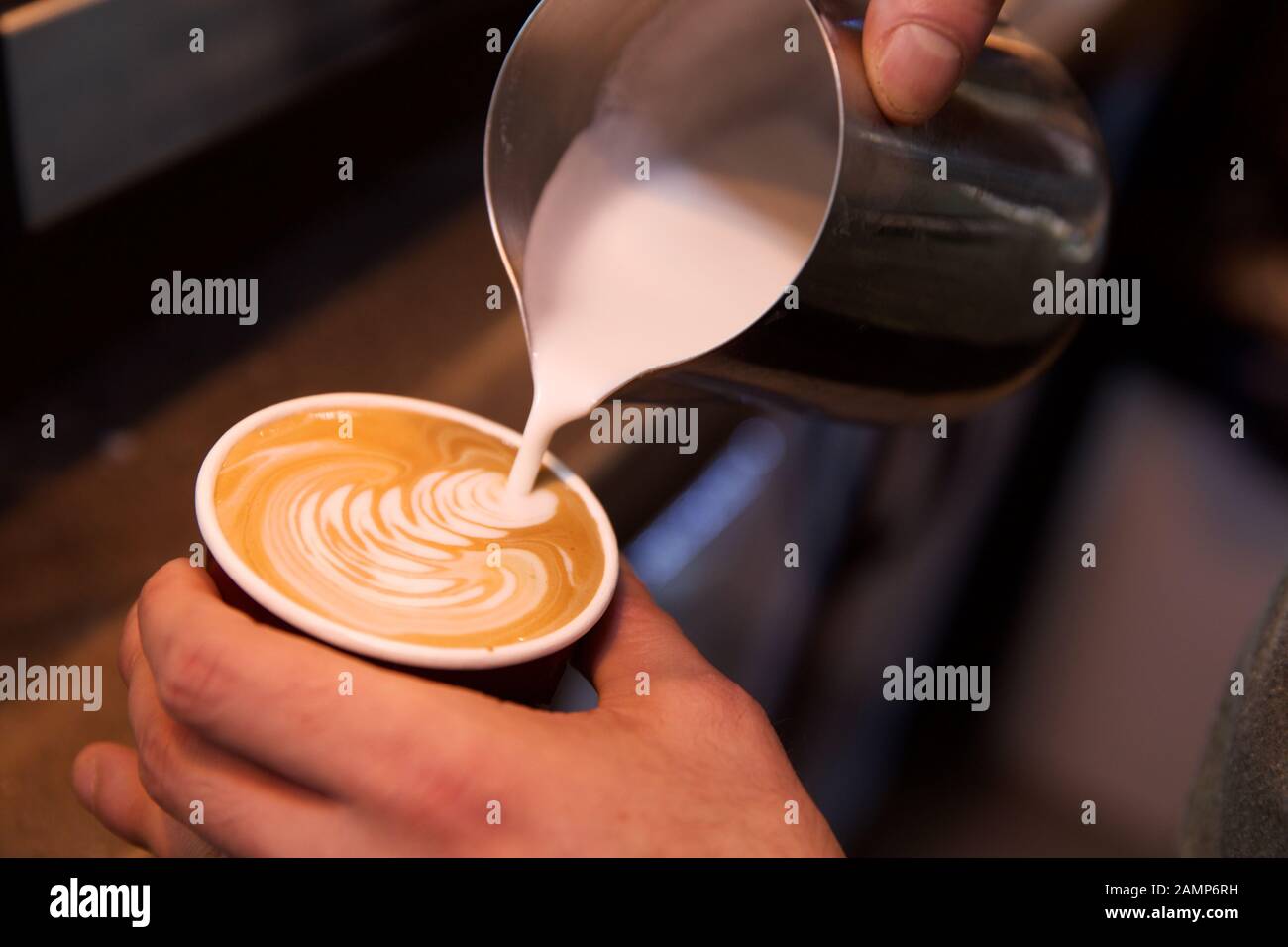 Close up of a barista adding foamed milk to a coffee. Stock Photo