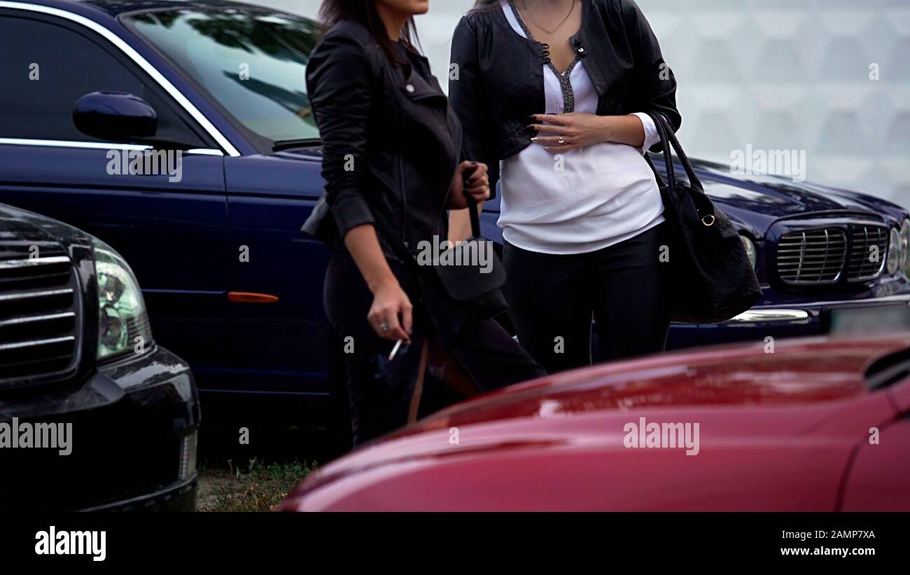 Two slim women smoking cigarettes on parking lot next to club, girltime break Stock Photo