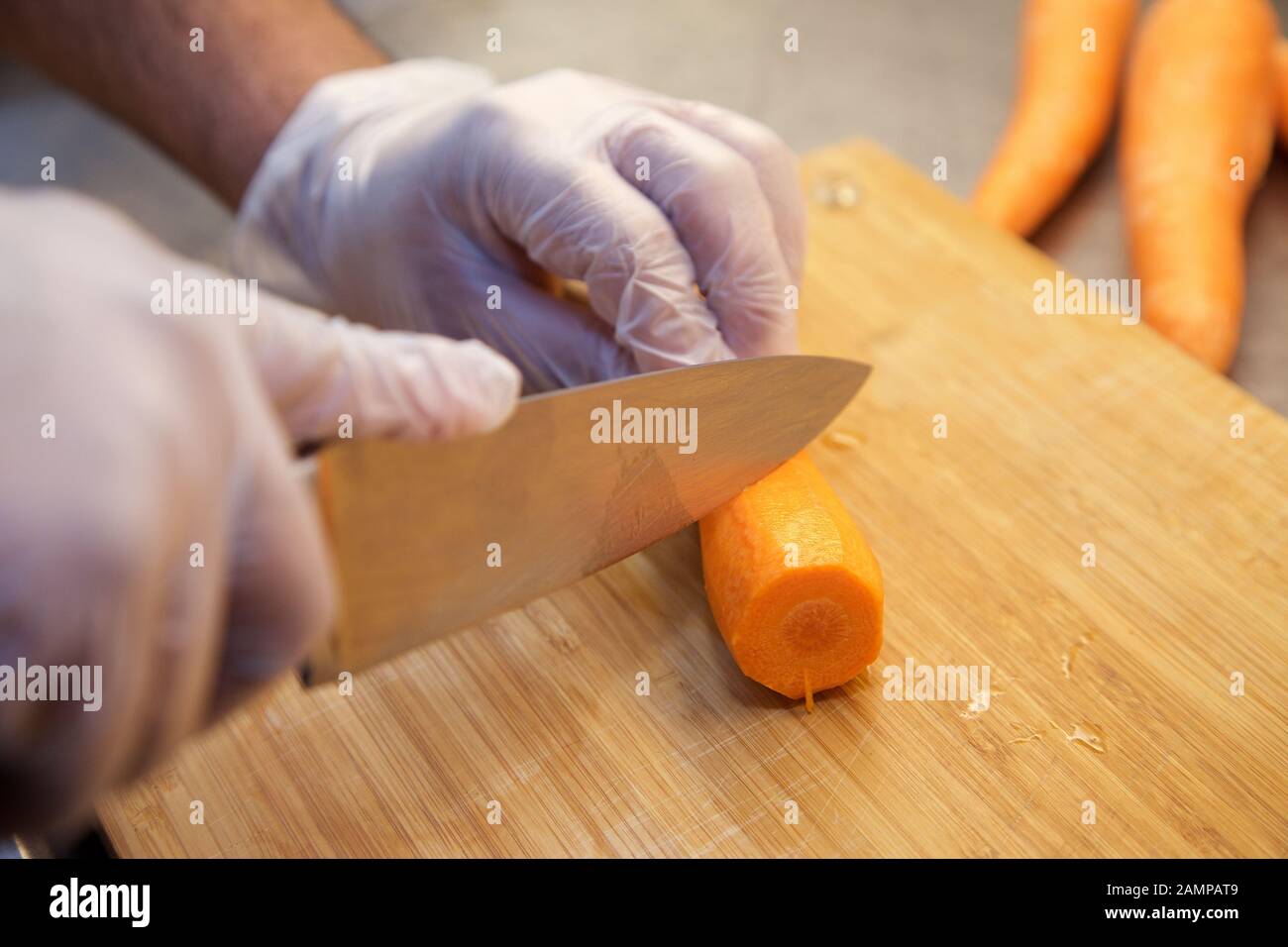 Close up shot of a chef chopping carrots on a wooden chopping board. Stock Photo