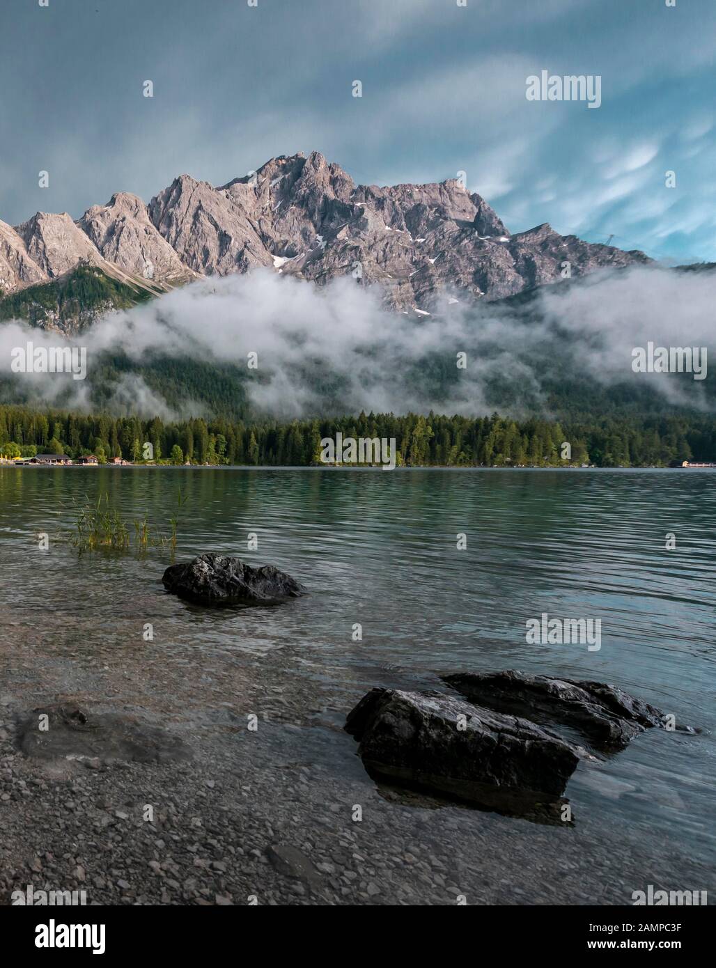 Rocks on the shore, Eibsee lake in front of Zugspitze massif with Zugspitze, low hanging clouds, Wetterstein range, near Grainau, Upper Bavaria Stock Photo