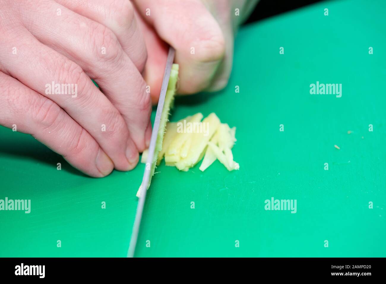 Close-up of a chef slicing ginger on a green chopping board. Stock Photo