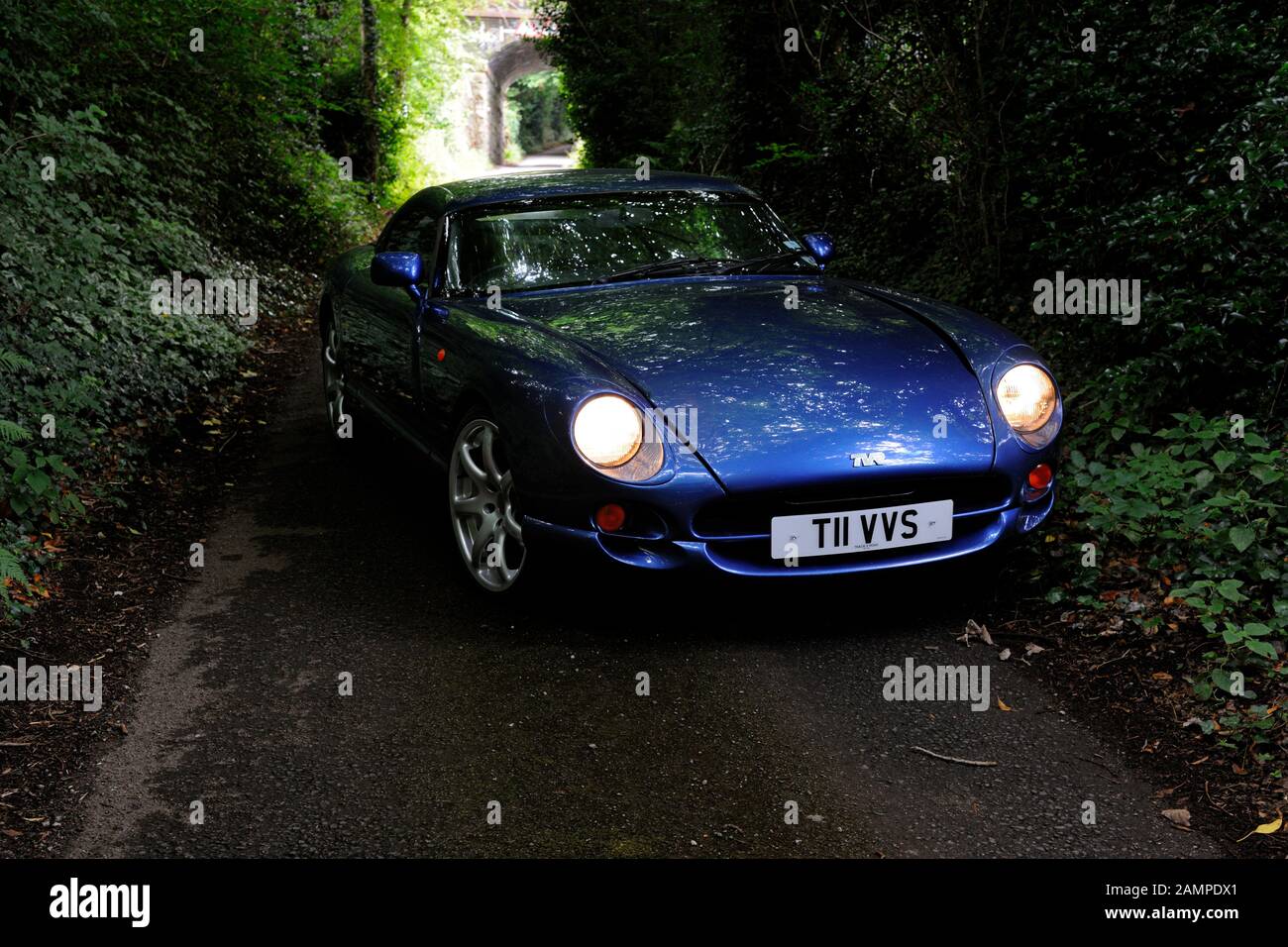 British TVR Cerbera muscle car parked in a dark and leafy country lane with its headlights on and a bridge behind Stock Photo