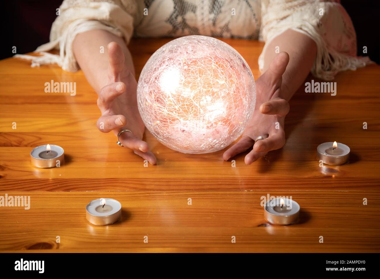 Fortune Teller with Crystal Ball on table with candles and black and red mottled background Stock Photo