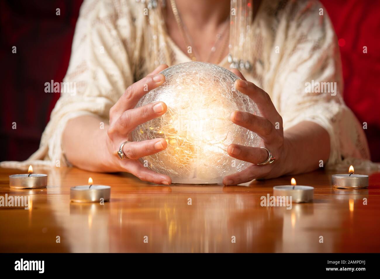 Fortune Teller with Crystal Ball on table with candles and black and red mottled background Stock Photo