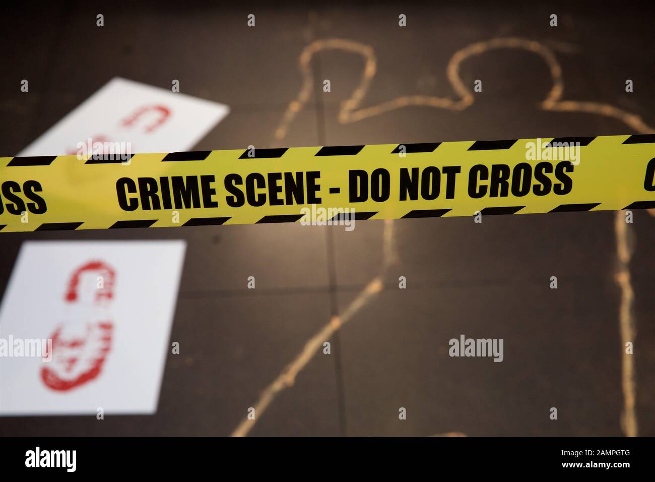Mock crime scene with yellow police cordon ribbon and chalk body outline. Stock Photo