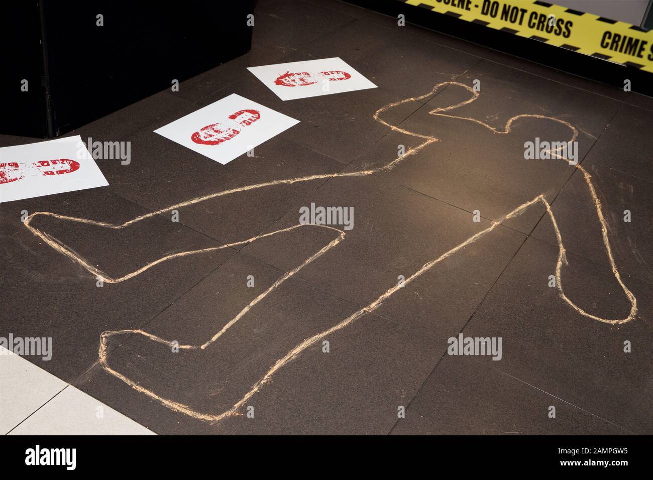 Mock crime scene with yellow police cordon ribbon and chalk body outline. Stock Photo