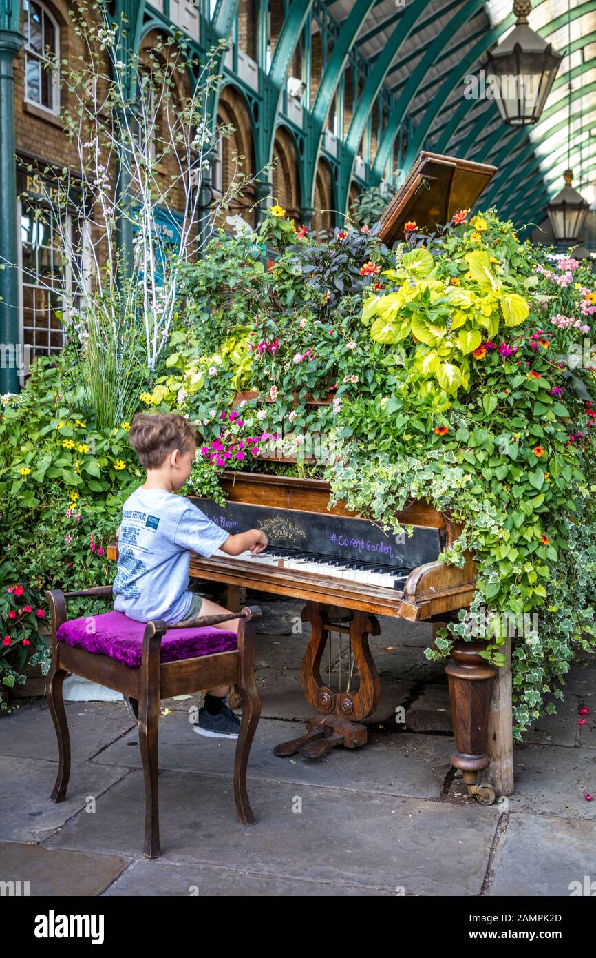 Young boy playing plant-covered grand piano on display at Covent Garden, London, England, UK Stock Photo