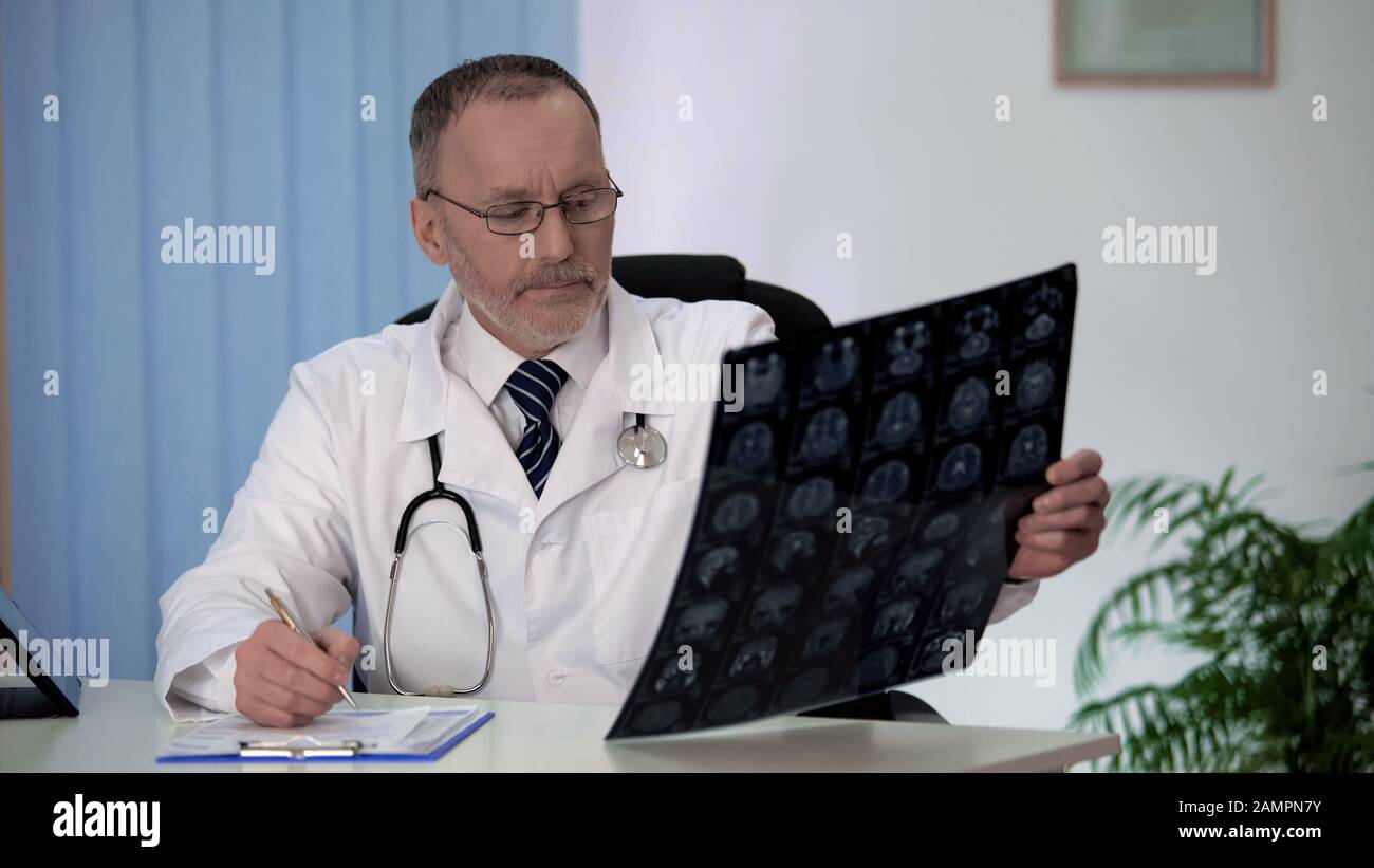 Neurologist carefully studying brain MRI, disturbed by results, making notes Stock Photo